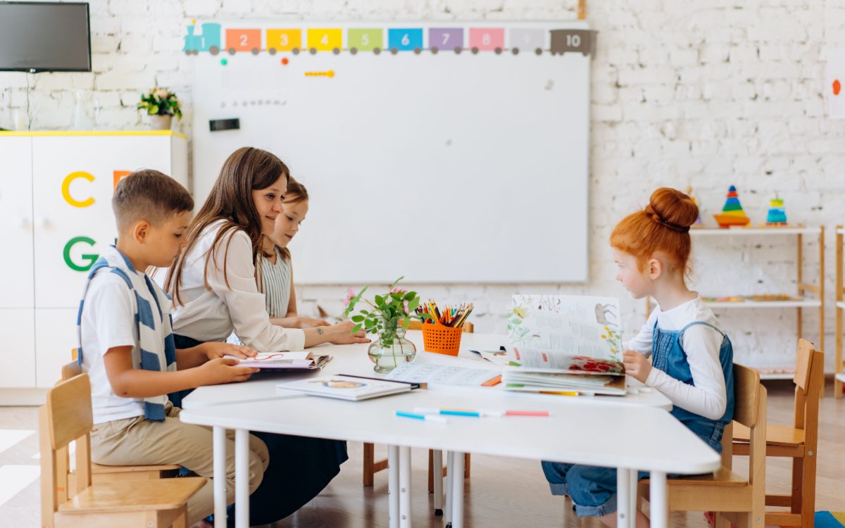 Trainerin arbeitet mit Kindern an einem Tisch im hellen Klassenraum